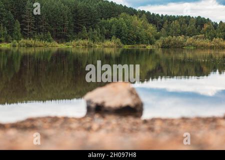Natural landscape of the lake, high resolution. Reflection of clouds on water ripples. The shore of the lake is made of small stones. In the foregroun Stock Photo