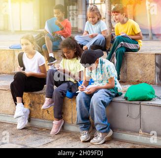 Tweenagers studying outside school, writing in workbooks Stock Photo
