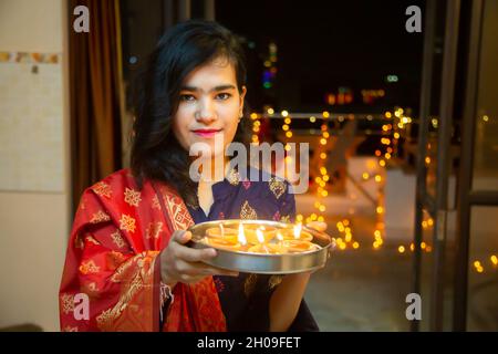 Portrait of Happy Young indian girl  celebrating diwali festival at home. Female standing with plate with oil lamps looking at camera. Stock Photo