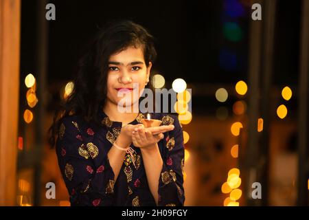 Portrait of Happy Young indian beautiful woman holding diya/clay oil lamps wearing traditional dress,celebrates diwali,at home,indoor.Gorgeous female Stock Photo