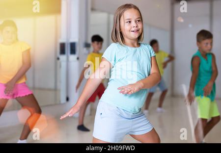 Cheerful preteen girl learning energetic dance in choreography class Stock Photo