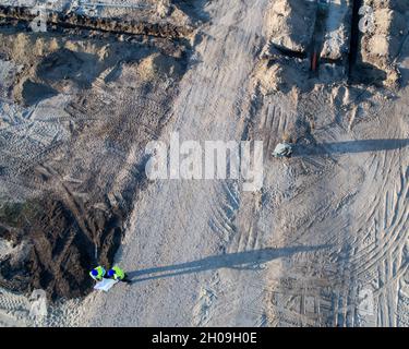 Aerial image of two engineers with helmets and vests, holding blueprints on construction site. Shoot from drone Stock Photo