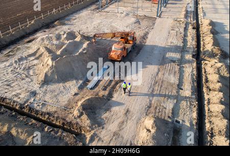 Aerial image of two engineers with helmets and vests, holding blueprints on construction site. Shoot from drone Stock Photo
