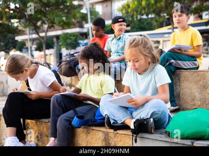 Tweenagers studying outside school, writing in workbooks Stock Photo