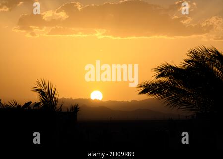 Dramatic colorful sky over silhouettes of trees and mountain at sunset Stock Photo