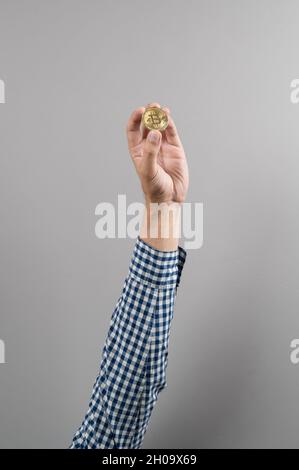 Close up of man holding gold coin of Bitcoin over gray background. Digital Money within the blockchain network Stock Photo