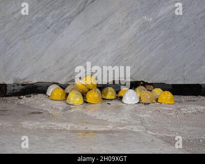 Yellow Work Protective Helmets Resting on the Ground in front of a Marble Slab: Marble Quarry Workers. Stock Photo