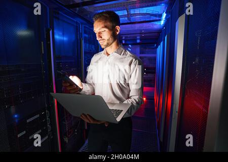 Man IT technician inspecting server with laptop in data center Stock Photo