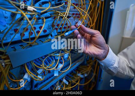 Technician plugging in optical fiber into server rack switch Stock Photo