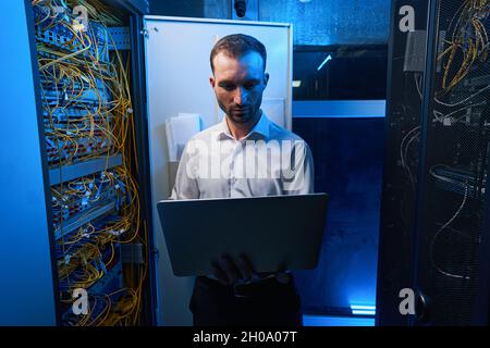 Man using laptop near open server cabinet Stock Photo