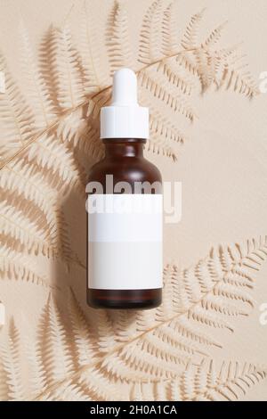 dark amber glass bottle with oil with fern on beige background. Beauty concept, minimalism brand packaging mock up. Stock Photo
