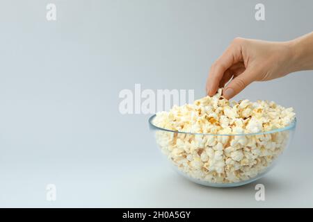 Female hand take popcorn from bowl on light gray background. Stock Photo