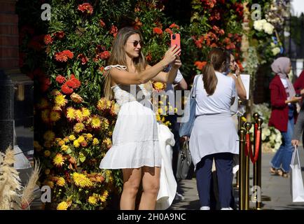 Young woman taking a selfie on her mobile during Chelsea in Bloom annual floral art show and flower shower in the shops and streets of Chelsea put on Stock Photo