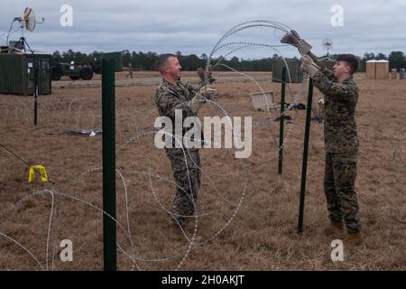 US Marine Corps Staff Sgt. Geoffrey A. Childers (left), an Imagery analysis specialist, and Lance Cpl. Zachery D. Larock (right), an unmanned aerial systems operator, install Concertina wire in preparation for exercise Black Shadow at Fort Stewart, Georgia, January 12, 2021. Marines with Unmanned Aerial Vehicle Squadron 2 (VMU-2) trained with soldiers with the Combat Aviation Brigade, 3rd Infantry Division in an unfamiliar environment in order to increase proficiency in critical mission skills such as aerial reconnaissance, convoy escort, and support of close air support. VMU-2 is a subordinat Stock Photo