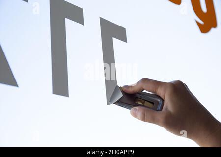 Close up of a Woman hand removing a vinyl sticker from a window with a scraper tool Stock Photo