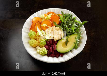 From above of vegetarian Buddha bowl with fresh assorted vegetables and hummus served on black table for healthy lunch Stock Photo