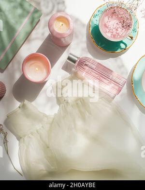 Women morning routine with tea, candles, facial toner in glass bottle, clothes, flowers and notepad on white background. Cozy morning at home with bea Stock Photo