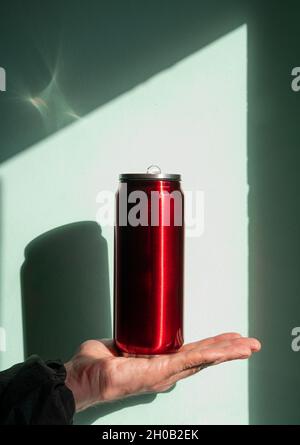 Red thermo can bottle in male hands blue turquoise wall background harsh shadow. Hot tea coffee beverages drinking in cold autumn winter weather. Dura Stock Photo