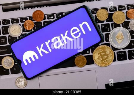 Kraken is cryptocurrency exchange. A smartphone with the Kraken logo metal coins, bitcoin, ethereum on a laptop keyboard. Stock Photo