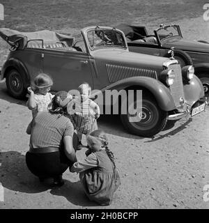 Eine Frau mit drei kleinen Mädchen auf einem Parkplatz vor einem Mercedes Benz 170 V (W 136) in Freudenstadt im Schwarzwald, Deutschland 1930er JAhre. A woman with three toddler girls in front of a Mercedes Benz 170 V (W 136) at Freudenstadt in Black Forest, Germany 1930s. Stock Photo