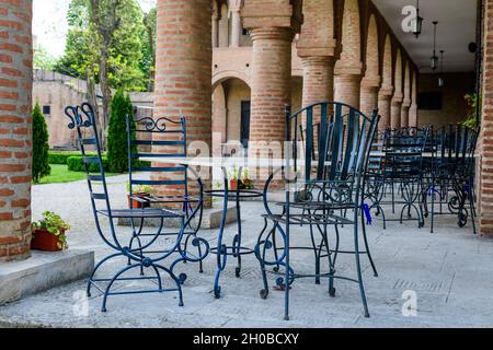 Elegant black metallic chairs and one white table near a red bricks wall in a garden in a sunny spring day, in Bucharest, Romania Stock Photo