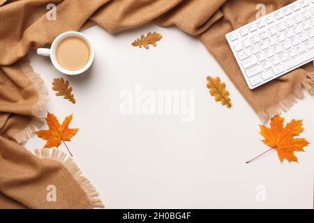 Autumn workplace coziness composition concept. Cashmere scarf keyboard coffee cup with autumn maple and oak leaves on a light gray background. Flat la Stock Photo