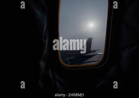 The sun rises on the flight line, masked by fog, seen from inside a U.S. Air Force KC-135 Stratotanker aircraft stationed at Al Udeid Air Base, Qatar, Jan. 05, 2021. Because of a specific mixture of atmospheric conditions, it’s extremely difficult to forecast the appearance of fog on Al Udeid AB. In order to prevail tomorrow, base personnel utilize specific risk assessments before returning to air and ground operations, ensuring the safety of personnel and assets in lowered visibility conditions. Stock Photo