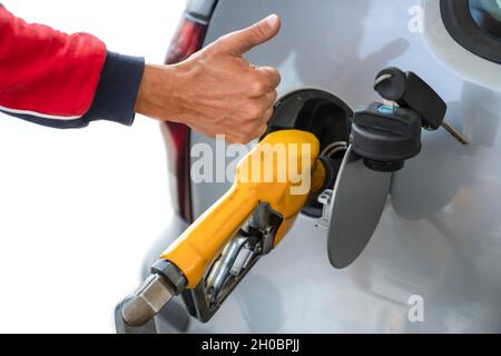 Man's hand with raised finger up, next to refueling gun, while refueling car with gasoline fuel -concept of high-quality service and fuel. Close-up. Stock Photo