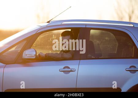 Handsome young man driving car and looking through window at sunset Stock Photo