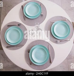Kitchen table setting with turquoise plates and glasses. Cutlery on white table, interior Stock Photo