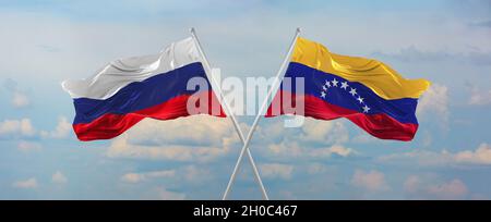 flags of Russia and Venezuela waving in the wind on flagpoles against sky with clouds on sunny day. Symbolizing relationship, dialog between two count Stock Photo