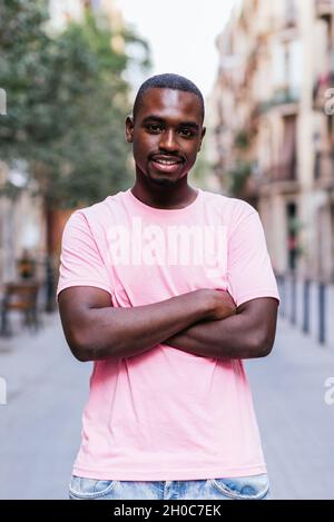vertical portrait of an african young man. He is looking at camera and smiles while standing in the streets of Barcelona Stock Photo