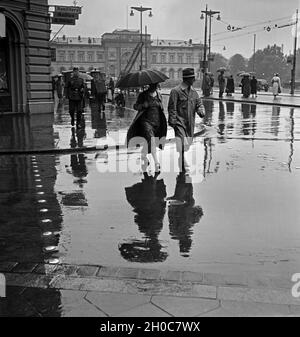 Menschen eilen im Regen auf dem Platz vor dem Hauptbahnhof in Braunschweig, Deutschland 1930er Jahre. People in a hurry on the square in front of Braunschweig main station, Germany 1930s. Stock Photo