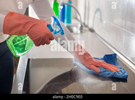 Close up of female hands with protective gloves spraying induction stove and cleaning with wipe in kitchen