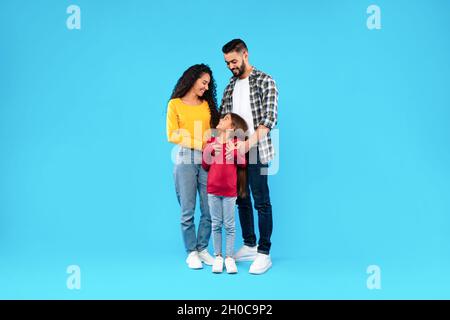 Middle-Eastern Parents Embracing Their Happy Daughter On Blue Background Stock Photo