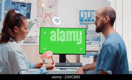 Oral care team looking at horizontal green screen on monitor while analyzing layout of teeth for dental examination. Assistant and dentist using tools and chroma key with mockup template Stock Photo