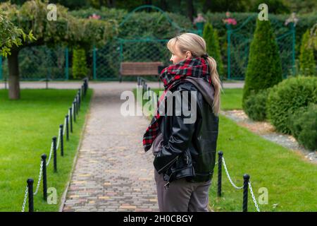 Stylish blond woman in black leather jacket walking in the park. A beautiful fashionable woman. Lifestyle concept. Stylish casual clothes. Stock Photo