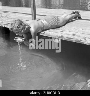 Eine junge Frau liegt auf einem Holzsteg und trinkt Wasser aus einem See in Österreich, 1930er Jahre. A young woman lying on a landing stage and drinking water from a lake in Austria, 1930s. Stock Photo