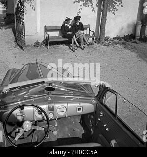 Zwei Frauen sitzen vor einem Eingangstor auf einer Bank, davor der geparkte Opel Olympia, Österreich 1930er Jahre. Two women on a bench in front of an entrance, a parked Opel Olympia in front of them, Austria, 1930s. Stock Photo