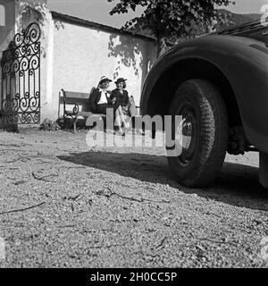 Zwei Frauen sitzen vor einem Eingangstor auf einer Bank, davor der geparkte Opel Olympia, Österreich 1930er Jahre. Two women on a bench in front of an entrance, a parked Opel Olympia in front of them, Austria, 1930s. Stock Photo
