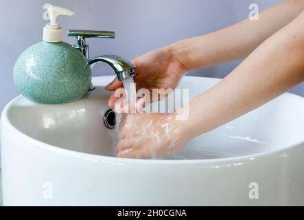 https://l450v.alamy.com/450v/2h0cgna/washing-hands-in-a-round-white-ceramic-basin-soap-bubbles-on-hand-there-is-a-green-liquid-soap-bottle-on-the-basin-and-water-is-flowing-from-the-tap-2h0cgna.jpg