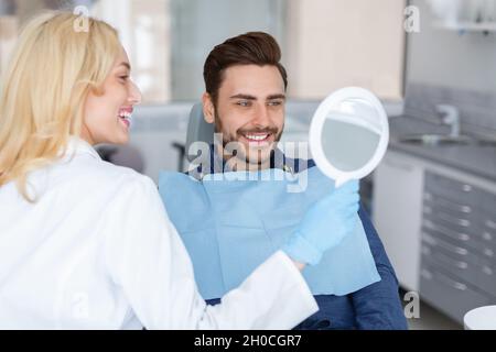 Cheerful woman doctor holding mirror for happy man patient Stock Photo