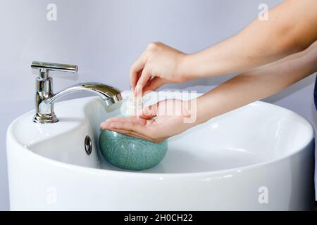 Hand pressing a bottle of hand soap pump on a clean white round sink, copy space. Stock Photo