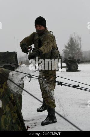 A U.S. Army Soldier, from the Wisconsin National Guard 120th Field Artillery Regiment, shovels snow while setting up a tent during Northern Strike 21-1/”Winter Strike 21” Jan. 24, 2021, at Camp Grayling Maneuver Training Center, Michigan. Winter Strike is a cold-weather joint fires military readiness exercise, which is held at the National All-Domain Warfighting Center in Northern Michigan. Stock Photo