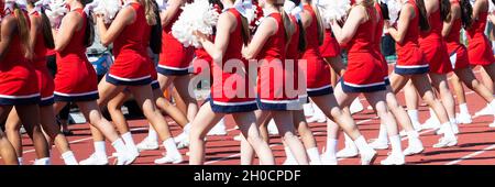 High school cheerleaders wearing red and white uniforms cheering while holding pom poms during a homecoming football game. Stock Photo
