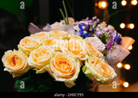 Bouquet of tea roses flowers on a dark background in a loft with warm lights on. The focus is on the foreground. Stock Photo