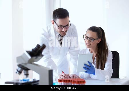 Man and woman scientists looking at tablet and analyzing data from microscope test Stock Photo