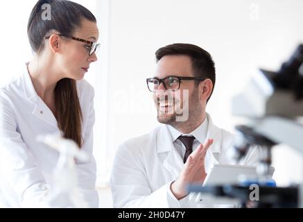Man and woman scientists analyzing data from microscope test Stock Photo
