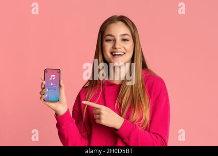 Cheerful Teen Female Pointing At Smartphone With Opened Music Player On Screen Stock Photo