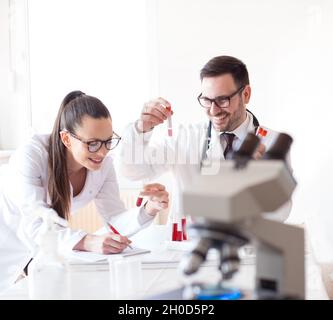 Man and woman scientists looking at tablet and analyzing data from microscope test Stock Photo